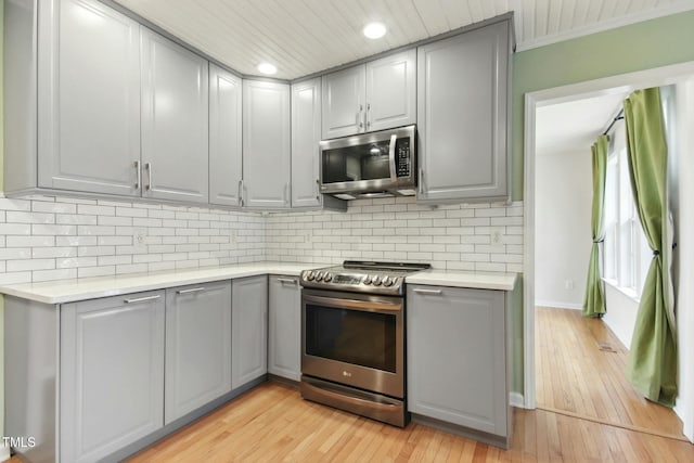 kitchen featuring stainless steel appliances, ornamental molding, backsplash, gray cabinets, and light wood-type flooring