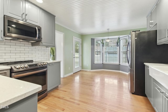 kitchen with stainless steel appliances, decorative backsplash, gray cabinetry, light wood-type flooring, and decorative light fixtures