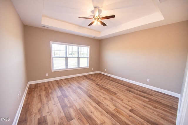 unfurnished room with a tray ceiling, ceiling fan, and wood-type flooring