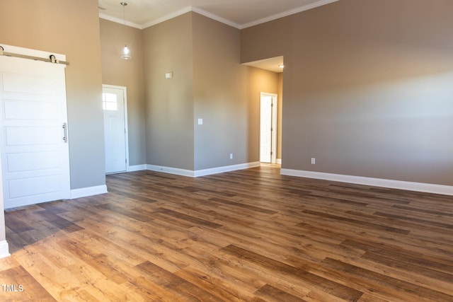 empty room with a barn door, dark hardwood / wood-style flooring, a towering ceiling, and ornamental molding