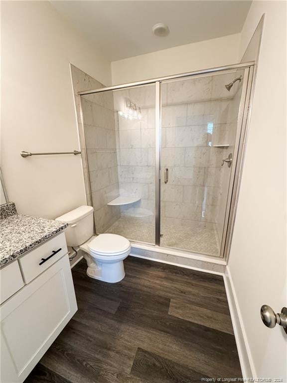 bathroom with toilet, vanity, wood-type flooring, and a shower with door