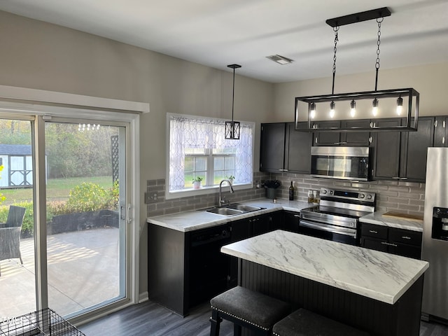 kitchen with stainless steel appliances, a kitchen island, dark hardwood / wood-style floors, hanging light fixtures, and sink