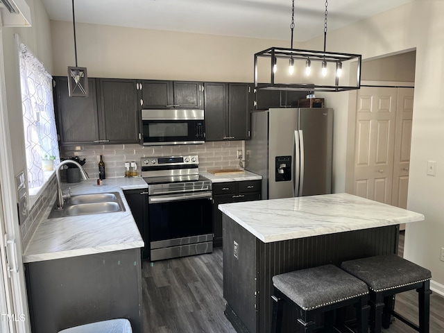 kitchen with stainless steel appliances, backsplash, decorative light fixtures, sink, and dark wood-type flooring