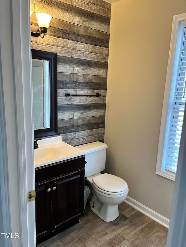 bathroom featuring wood-type flooring, wooden walls, toilet, and vanity