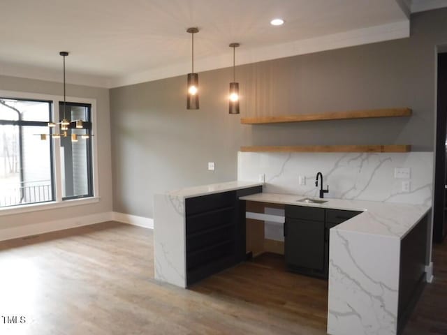 kitchen featuring backsplash, light stone counters, sink, decorative light fixtures, and light hardwood / wood-style floors