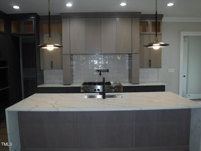 kitchen featuring gray cabinets, light stone countertops, backsplash, and a kitchen island with sink