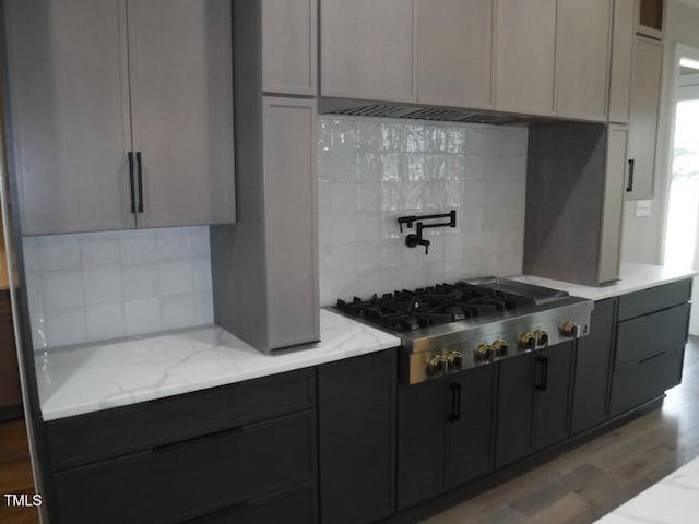 kitchen featuring gray cabinetry, light stone countertops, stainless steel gas cooktop, backsplash, and hardwood / wood-style flooring