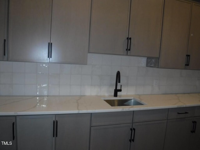 kitchen featuring tasteful backsplash, gray cabinetry, light stone counters, and sink