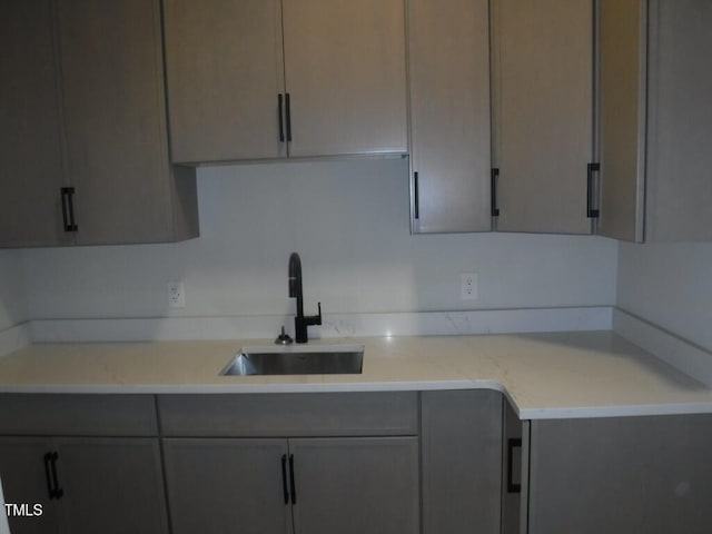 kitchen featuring light stone counters, gray cabinetry, and sink