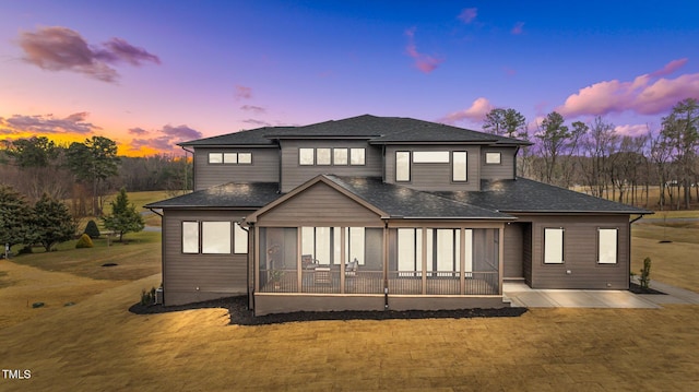 back house at dusk with a patio area, a sunroom, and a lawn