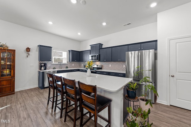 kitchen featuring a kitchen island, backsplash, a kitchen bar, stainless steel appliances, and light wood-type flooring