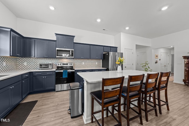 kitchen featuring a kitchen island, appliances with stainless steel finishes, light wood-type flooring, and a kitchen breakfast bar