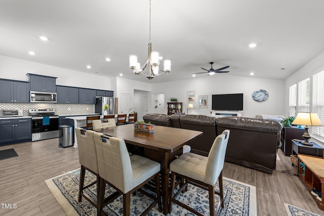 dining space with ceiling fan with notable chandelier, light hardwood / wood-style floors, and lofted ceiling