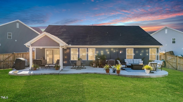 back house at dusk with outdoor lounge area, a patio, and a lawn