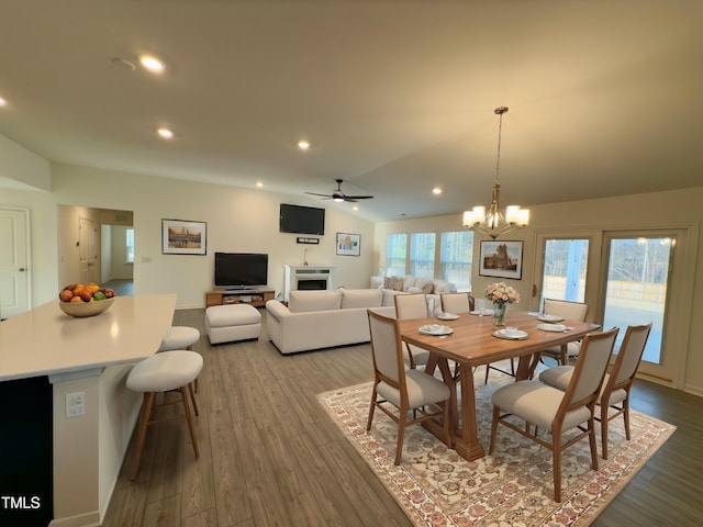 dining space with lofted ceiling, ceiling fan with notable chandelier, and light wood-type flooring