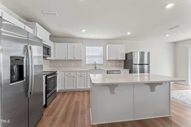 kitchen with stainless steel appliances, a center island, white cabinets, sink, and light hardwood / wood-style flooring