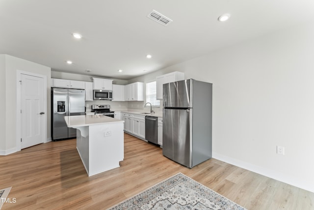 kitchen featuring light hardwood / wood-style floors, stainless steel appliances, a center island, white cabinets, and sink