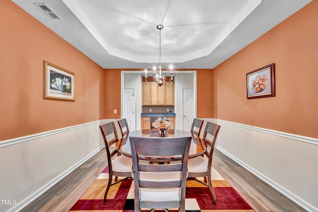 dining space featuring hardwood / wood-style floors, a raised ceiling, and a notable chandelier