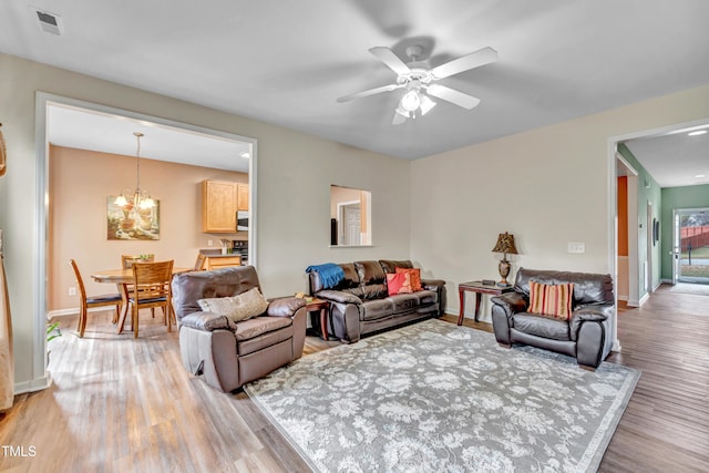 living room featuring light wood-type flooring and ceiling fan with notable chandelier