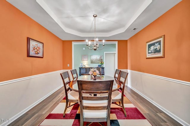 dining space featuring hardwood / wood-style floors, a raised ceiling, and an inviting chandelier