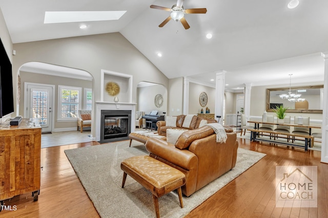 living room with ornamental molding, light wood-type flooring, ceiling fan with notable chandelier, and high vaulted ceiling