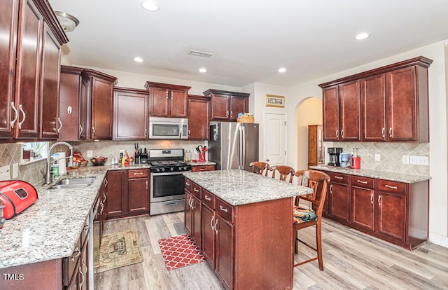 kitchen featuring appliances with stainless steel finishes, a center island, a kitchen breakfast bar, light wood-type flooring, and light stone counters