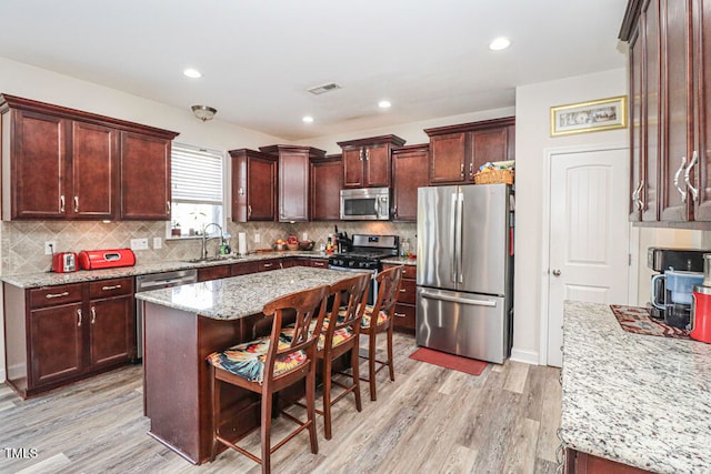 kitchen featuring sink, light stone countertops, a kitchen island, light hardwood / wood-style floors, and stainless steel appliances