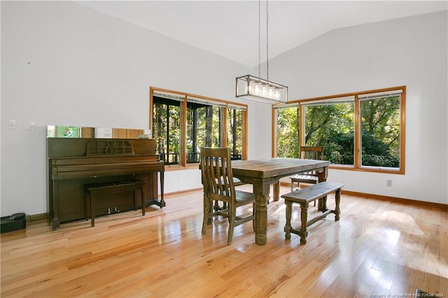 dining area with high vaulted ceiling, light wood-type flooring, an inviting chandelier, and plenty of natural light