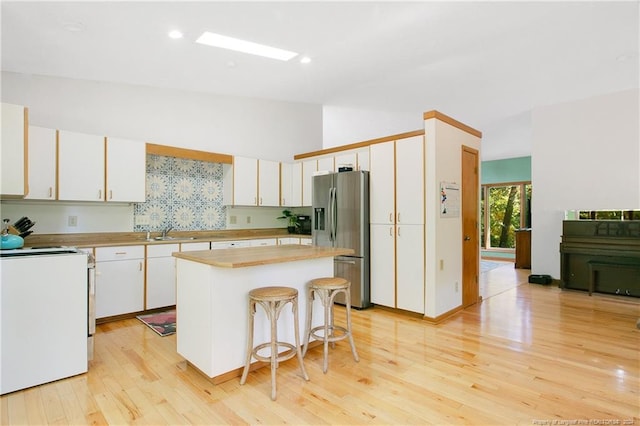 kitchen with a breakfast bar, a center island, white cabinets, stainless steel fridge, and light wood-type flooring