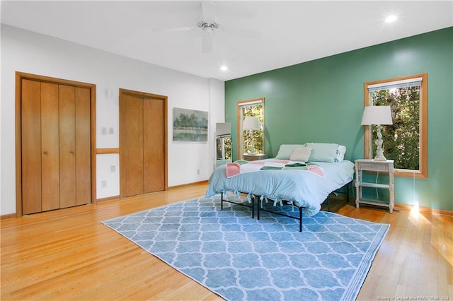 bedroom featuring hardwood / wood-style flooring, ceiling fan, and two closets