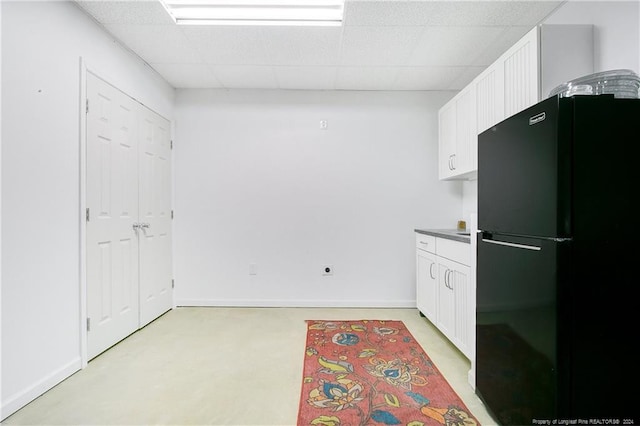 kitchen featuring white cabinetry, a drop ceiling, and black refrigerator