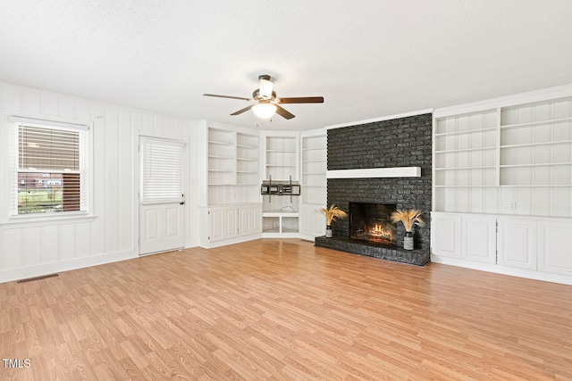 unfurnished living room with built in shelves, a textured ceiling, light hardwood / wood-style floors, and a brick fireplace