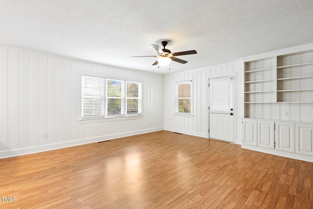 spare room featuring a textured ceiling, light wood-type flooring, ceiling fan, and built in shelves