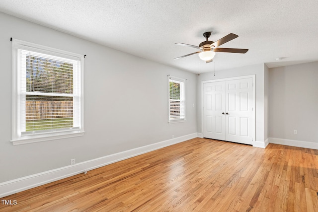 unfurnished bedroom with ceiling fan, light wood-type flooring, a textured ceiling, and multiple windows