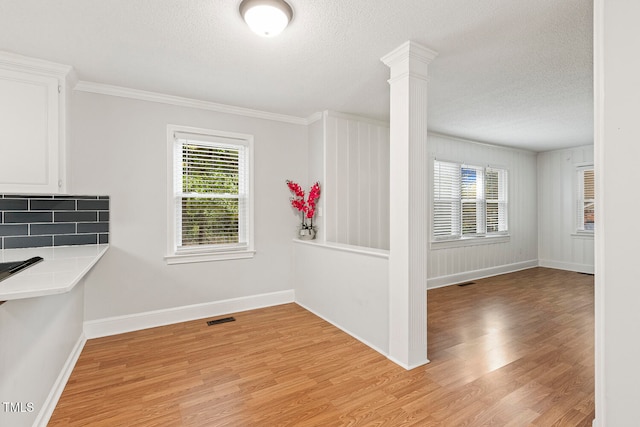 unfurnished dining area with a healthy amount of sunlight, decorative columns, a textured ceiling, and light hardwood / wood-style flooring