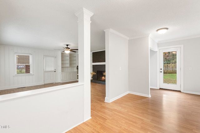 empty room featuring a fireplace, light wood-type flooring, decorative columns, and a healthy amount of sunlight