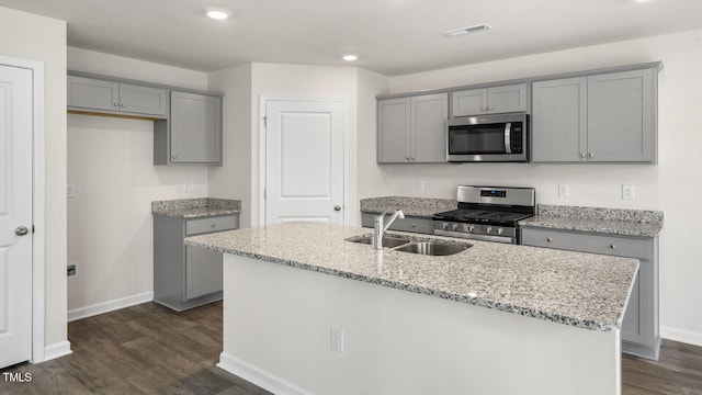 kitchen with stainless steel appliances, light stone counters, dark hardwood / wood-style floors, an island with sink, and gray cabinets