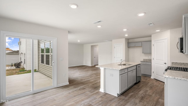 kitchen featuring hardwood / wood-style flooring, sink, light stone counters, an island with sink, and gray cabinetry