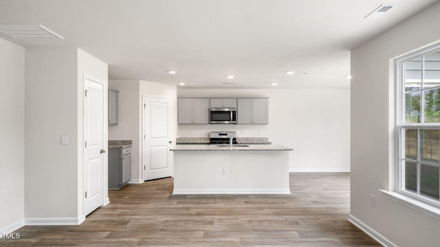 kitchen with gray cabinets, light wood-type flooring, appliances with stainless steel finishes, and an island with sink