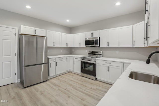 kitchen with white cabinets, light hardwood / wood-style floors, appliances with stainless steel finishes, and sink