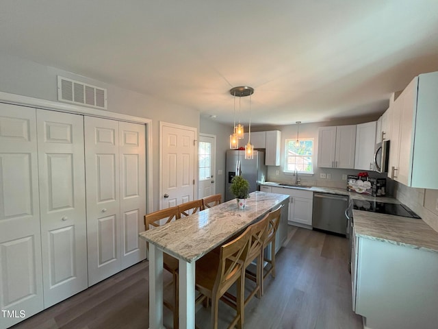 kitchen featuring appliances with stainless steel finishes, pendant lighting, sink, white cabinets, and dark hardwood / wood-style flooring