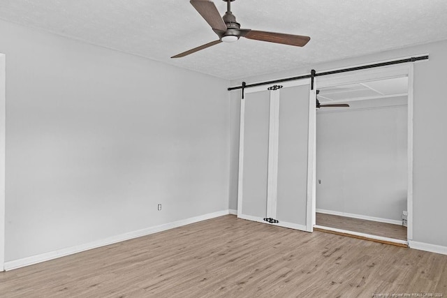 unfurnished bedroom with light hardwood / wood-style floors, a textured ceiling, a barn door, ceiling fan, and a closet