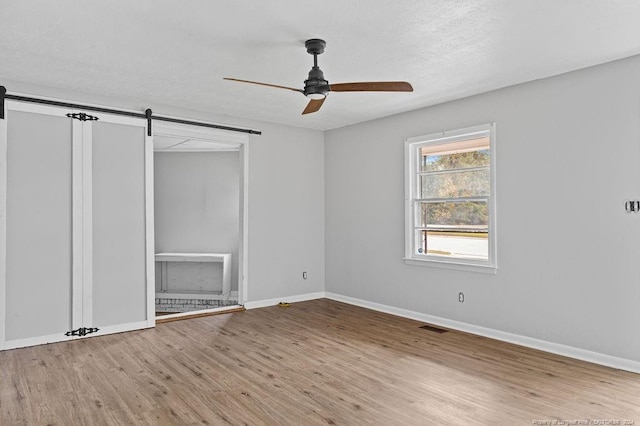 unfurnished bedroom with a textured ceiling, a barn door, ceiling fan, and light hardwood / wood-style flooring