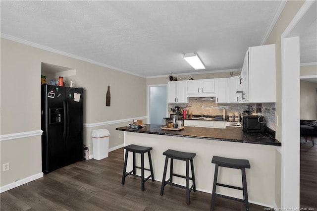 kitchen with black fridge, kitchen peninsula, ornamental molding, dark hardwood / wood-style floors, and white cabinets