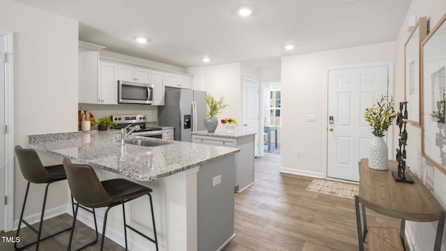 kitchen featuring stainless steel appliances, light stone counters, kitchen peninsula, hardwood / wood-style flooring, and white cabinetry