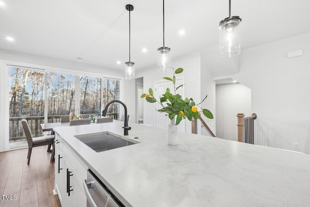 kitchen with stainless steel dishwasher, sink, light hardwood / wood-style flooring, white cabinets, and hanging light fixtures