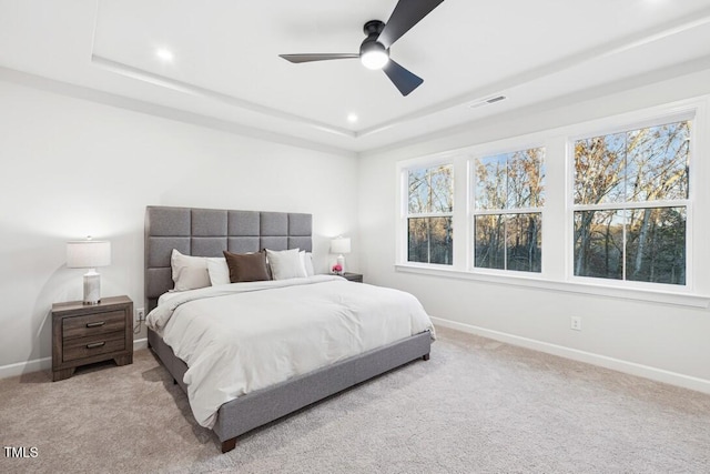 bedroom featuring a raised ceiling, ceiling fan, and light carpet