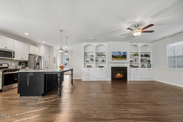 kitchen featuring appliances with stainless steel finishes, ceiling fan, decorative light fixtures, dark hardwood / wood-style floors, and an island with sink