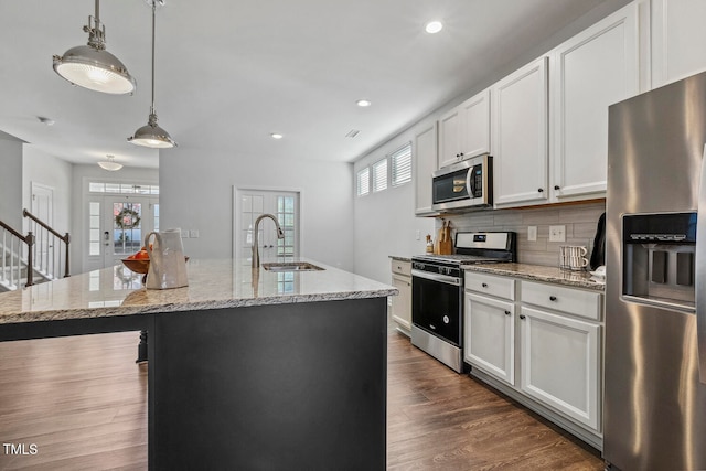 kitchen featuring stainless steel appliances, sink, pendant lighting, white cabinetry, and an island with sink