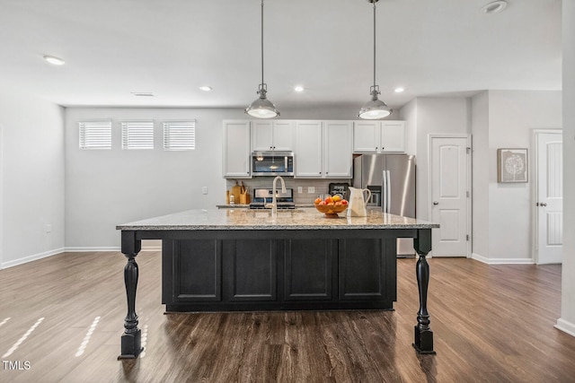 kitchen featuring light stone countertops, stainless steel appliances, an island with sink, decorative light fixtures, and white cabinets